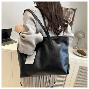 Detail of black large capacity leather tote bag worn as a shoulder bag in minimalist office