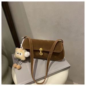 Close-up of brown suede shoulder bag with gold metal buckle and plush monster charm