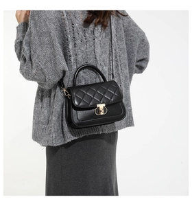 Detail of black quilted shoulder bag featuring gold circular metal clasp and top handle