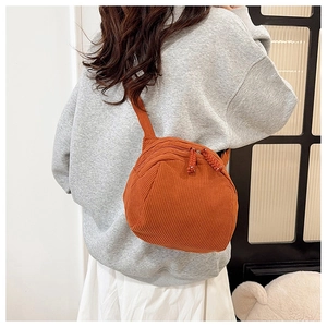Close-up of burnt orange corduroy crossbody bag texture and woven zipper pull detail