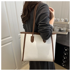 Detail of cream woven tote bag with brown leather handles and textured crocodile pattern