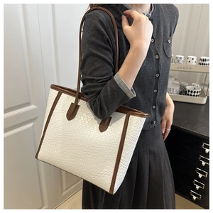 Close-up of white woven textured tote bag with brown leather straps and trim detailing