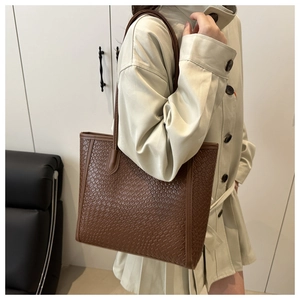 Detailed view of brown woven texture on a large capacity tote bag worn by a model