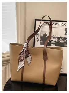 Detail of khaki leather tote bag with dark handles and a geometric pattern scarf accent