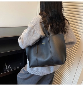 Gros plan d'un grand sac cabas noir en cuir avec logo doré porté à l'épaule d'un mannequin