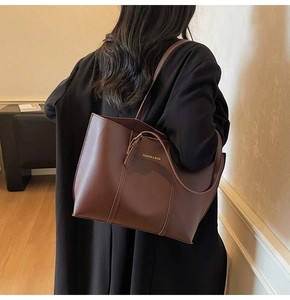 Detail of a dark brown leather tote bag worn by a model in a minimalist interior setting