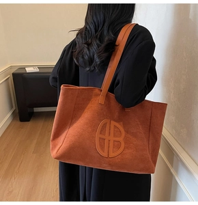 Detailed close-up of large suede tote bag with leather logo patch and long shoulder strap