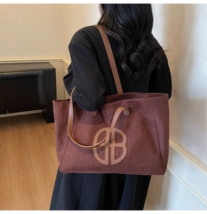 Detail of dark brown suede tote bag featuring a round logo and textured vintage finish