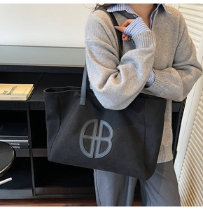 Detail of black canvas tote bag with circular logo and shoulder strap on model