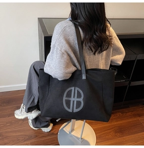 Detail of black canvas tote bag showing round double-B logo patch and shoulder strap