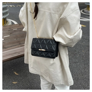 Close-up of black quilted leather handbag with gold chain strap worn over a beige coat