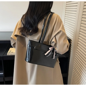 Dettaglio di borsa a spalla nera lucida con fiocco rosa e finitura in ecopelle chic