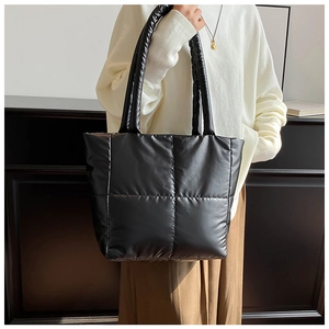 Chic black quilted puffer tote bag on model, featuring glossy finish and wide handles