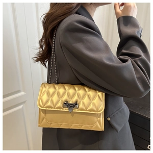 Detail of golden quilted crossbody bag with dark grey chain strap and metal lock buckle