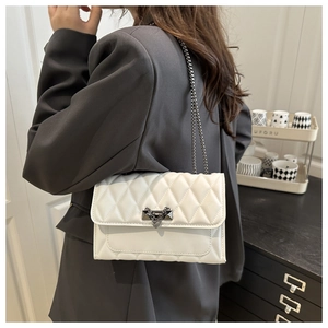 Detail of white quilted leather chain bag with metallic heart charm on a grey suit