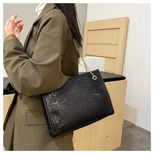 Détail du sac cabas noir à motif crocodile avec une élégante bandoulière dorée