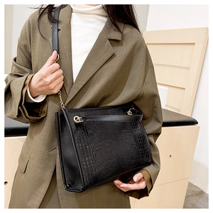 Détail du sac cabas noir à texture crocodile avec chaîne dorée sur une veste verte