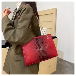 Détail du cabas rouge à texture crocodile avec chaînes dorées porté sur un tailleur vert