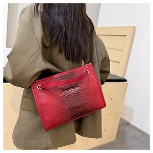 Détail d'un sac à main rouge motif crocodile avec poignée dorée et bandoulière chaîne