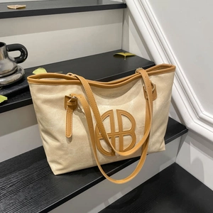 Large beige canvas tote bag with brown leather trim and circular logo on a black staircase