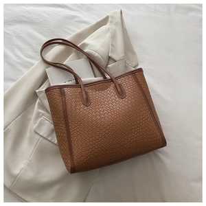 Détail d'un sac cabas marron tissé sur tissu blanc avec blazer beige et une carte