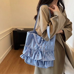 Blue and white gingham tote bag with ruffle hem and drawstring closure shown with trench coat