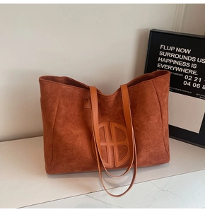 Detail of caramel brown suede tote bag featuring a round embossed logo and leather straps
