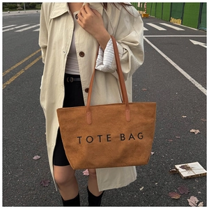 Brown suede tote bag with TOTE BAG lettering shown on model in beige trench coat