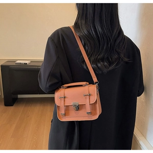 Detailansicht der orangeroten Retro-Tasche mit Metallschnalle auf schwarzem Blazer
