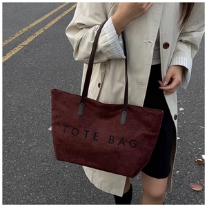 Macro detail of wine red suede tote bag texture with black printed lettering and leather straps