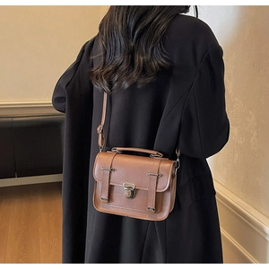 Nahaufnahme einer braunen Vintage-Ledertasche mit Silberschnalle über einem schwarzen Mantel