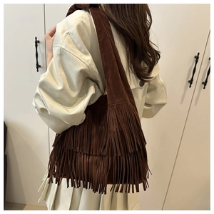 Detail view of brown fringe shoulder bag with long suede tassels on a beige coat