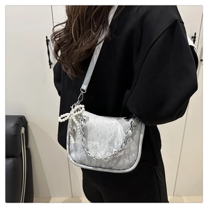 Détail du sac bandoulière argenté en croissant avec plis et pendentif nœud perlé