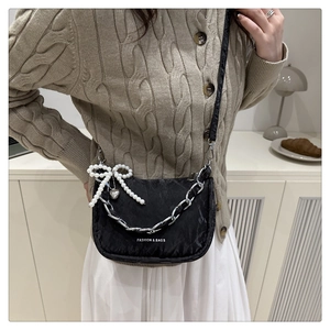 Détail d'un sac bandoulière noir avec chaîne argentée et pendentif nœud en perles