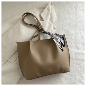Close-up of khaki tote bag with geometric scarf on handle against white background