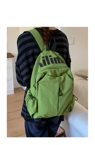 Green water-resistant nylon backpack with black letter print shown in a lifestyle setting