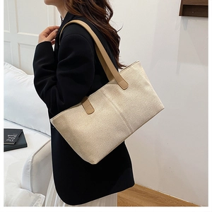 Detailed side view of a large beige canvas tote bag with brown leather handles