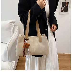 Detail of beige canvas tote bag with brown leather handles and teddy bear pendant