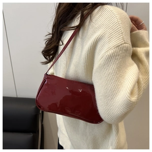 Detail showing high-gloss deep red patent leather shoulder bag worn by a model