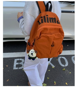 Outdoor view of orange water-resistant backpack with plush puppy charm and side pockets