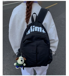 Detail of waterproof black backpack showing large white Aima print and cute dog plush charm