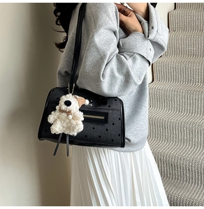Close-up of black patterned tote bag with a white plush bear charm and metal zipper detail