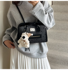 Polka dot denim shoulder bag with a plush puppy charm worn by a model in casual style