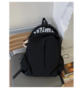 Detail of black waterproof nylon backpack featuring large white lettering and plush dog charm