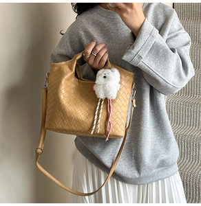 Close-up of woven shoulder bag in khaki with a cute plush bear pendant accessory
