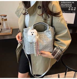 Silver woven handbag with white puppy plush charm shown by a model in lifestyle setting
