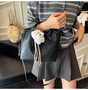 Detail of black woven crossbody bag with a plush puppy charm on a stylish model