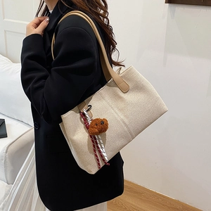 Large beige canvas tote bag with brown bear charm and red rope detail on shoulder