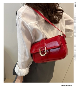 Detail of red patent leather shoulder bag with golden horseshoe buckle and flap closure