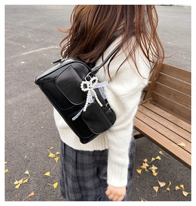 Détail d'un sac porté épaule noir mat avec nœud en perles et dentelle blanche